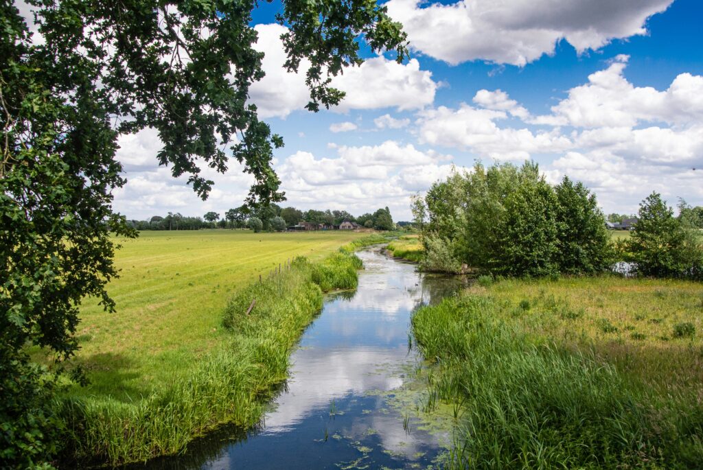 foto van beekje tussen weilanden, met wolkenlucht